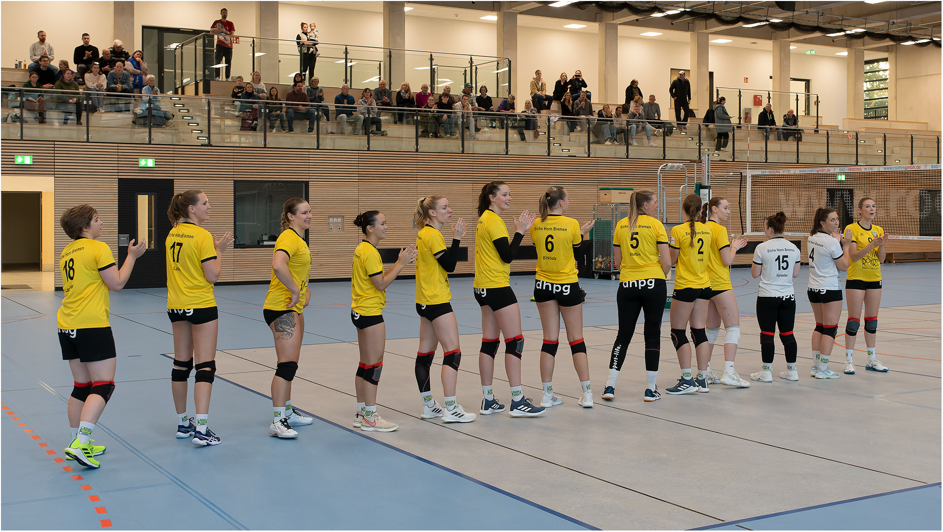 Das Volleyball Team steht in einer Reihe auf dem Spielfeld.